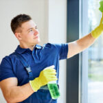 hombre joven limpiando ventanas pvc con producto en una mano y paño suave en otra mano